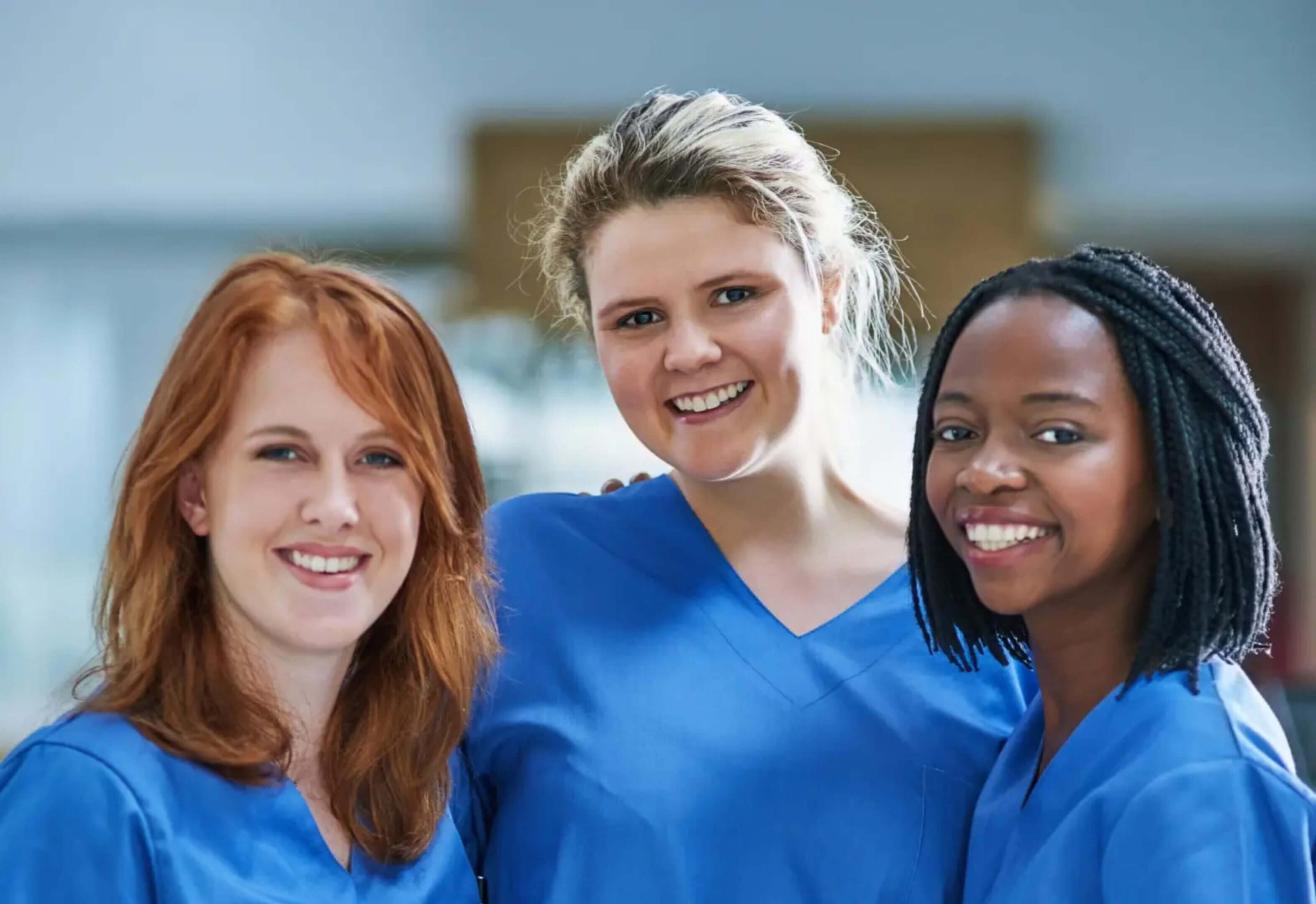 Three smiling healthcare professionals in blue scrubs.